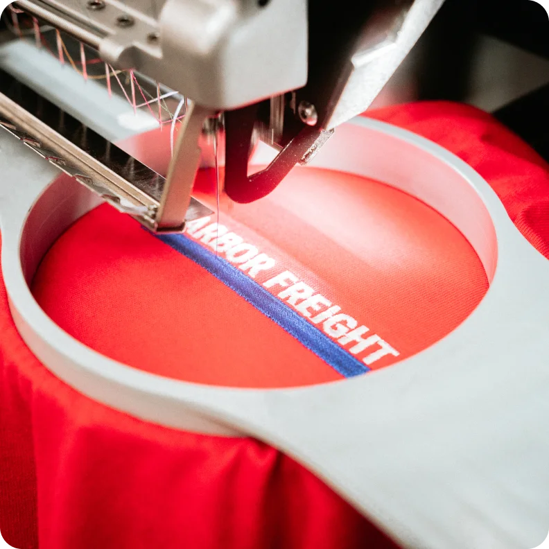 Embroidery machine stitching custom artwork onto red fabric.